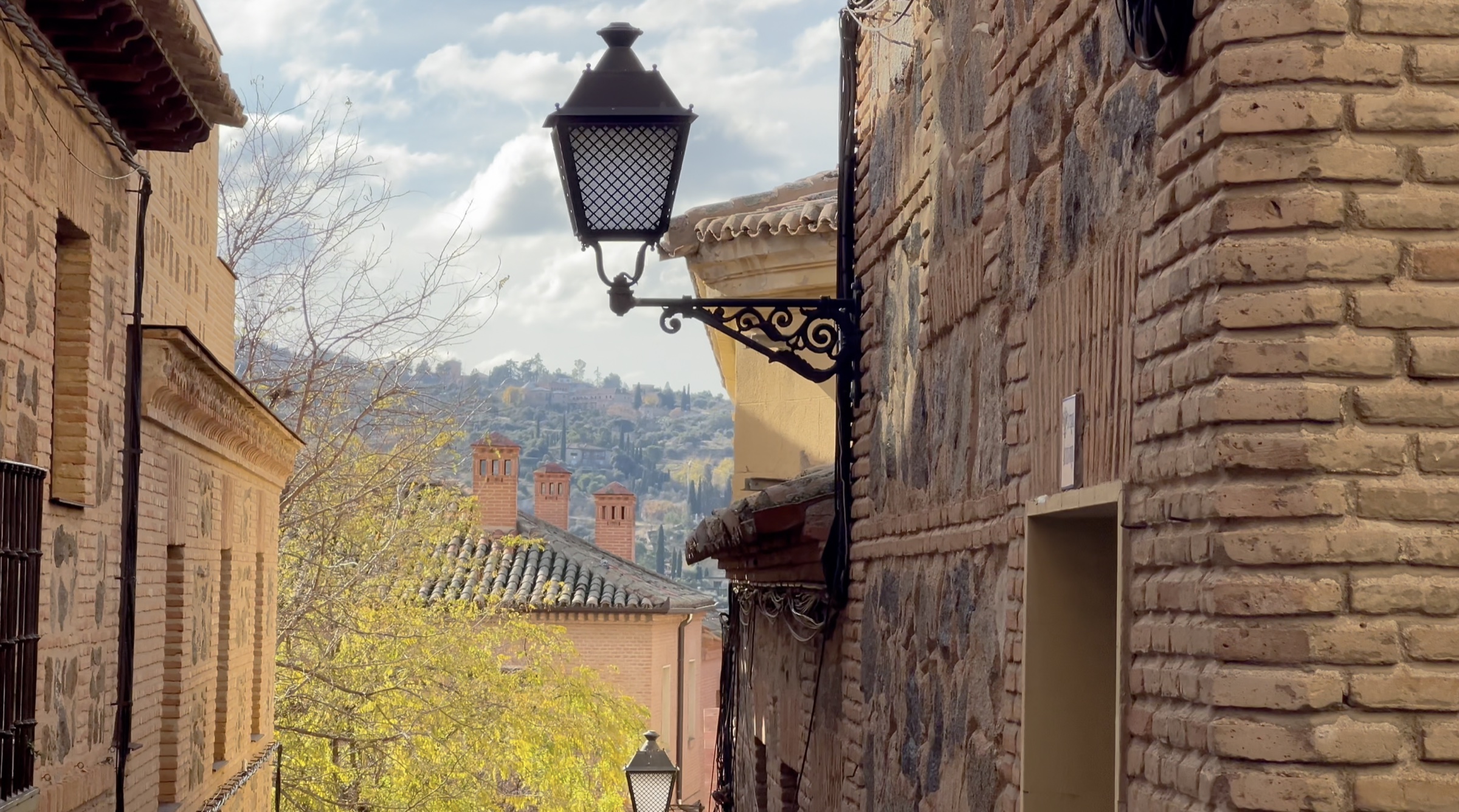 A wrought-iron street lamp on a brick wall in Toledo, with rooftops and hills beyond