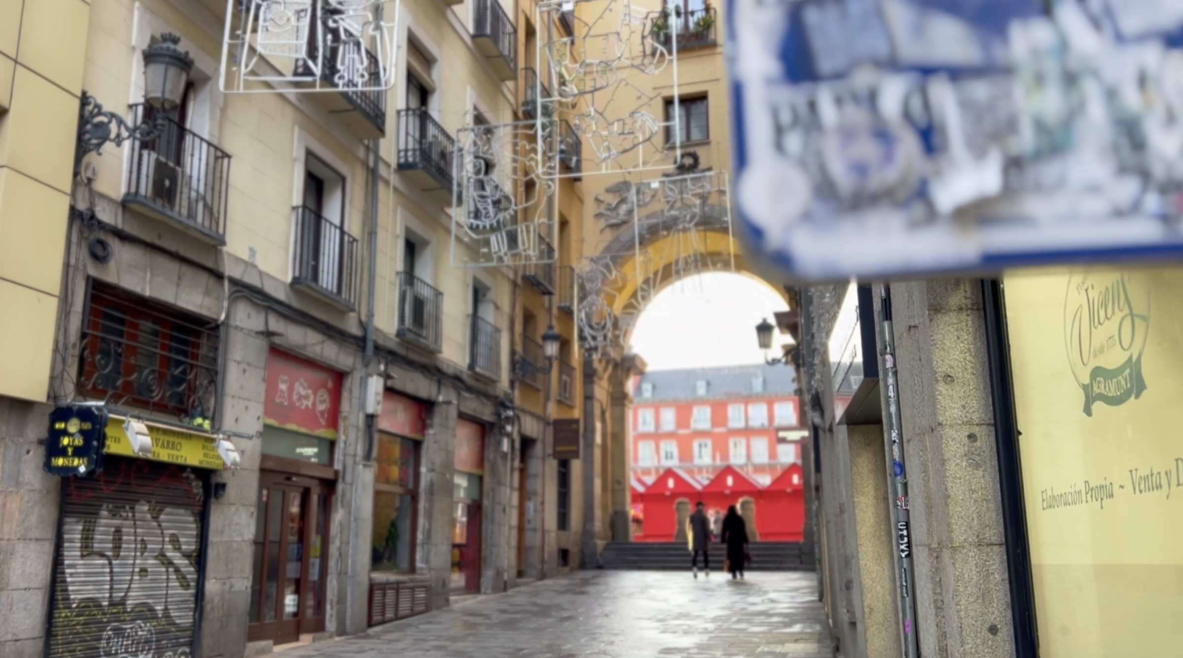 A Madrid side street opening onto a red-fronted building through an archway